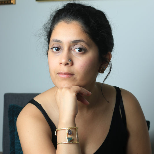 Woman wearing a black top with a gold bracelet, posing against a light blue wall.